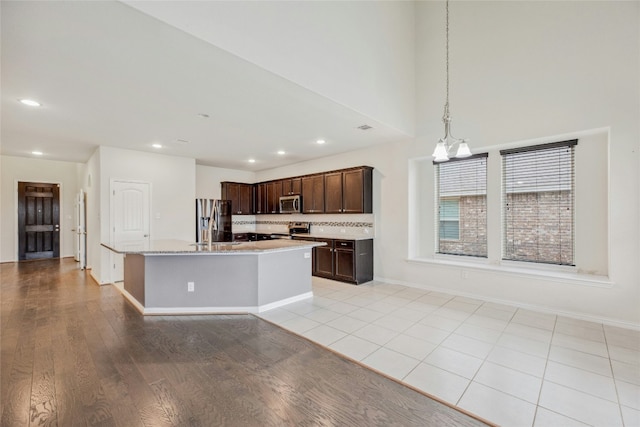 kitchen with appliances with stainless steel finishes, a kitchen island with sink, dark brown cabinets, pendant lighting, and a sink