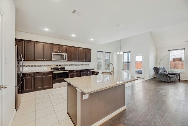 kitchen with stainless steel appliances, visible vents, backsplash, an island with sink, and light stone countertops