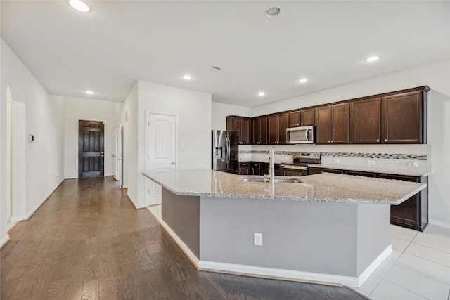 kitchen with light stone countertops, a center island with sink, stainless steel appliances, and a sink