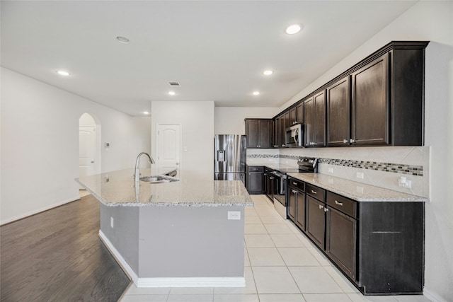 kitchen featuring a kitchen island with sink, arched walkways, stainless steel appliances, and a sink