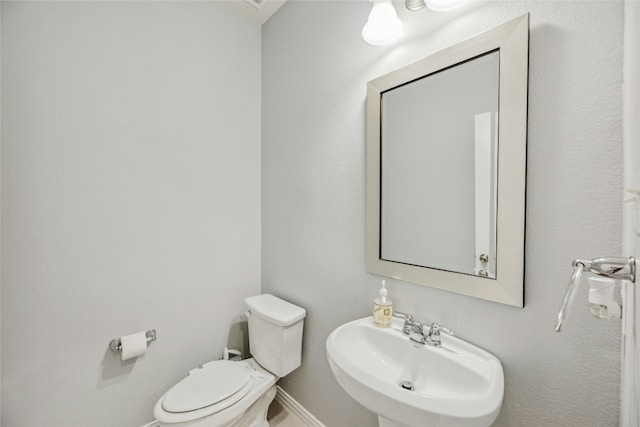 half bathroom with toilet, baseboards, and a sink