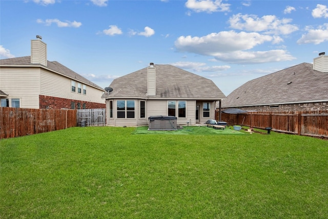 back of house with a chimney, a fenced backyard, a lawn, and a hot tub