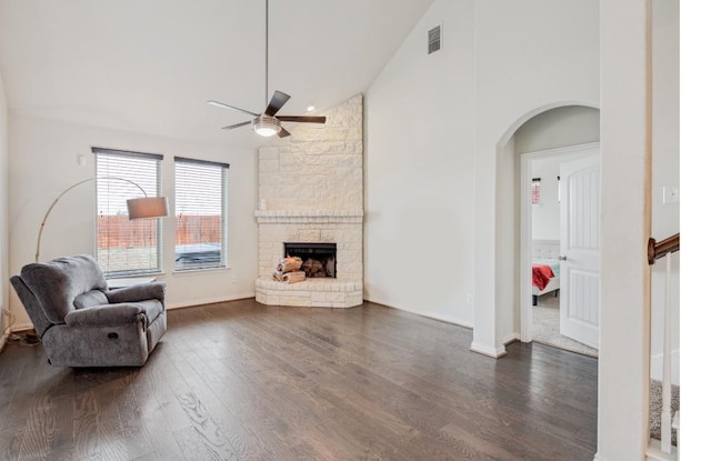 living room featuring arched walkways, high vaulted ceiling, a stone fireplace, dark wood-type flooring, and visible vents