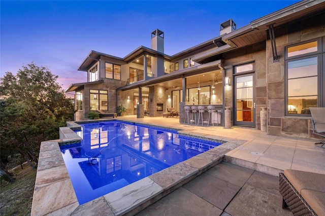 pool at dusk featuring a patio area and a bar