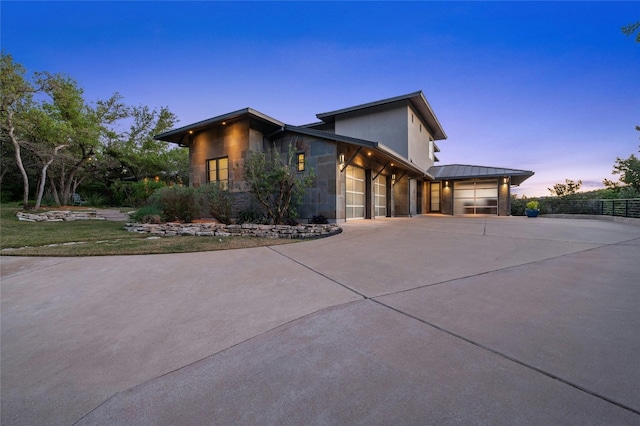 702 Crystal Mountain Dr, Austin, TX 78733 - property exterior at dusk featuring stone siding, concrete driveway, a garage, and stucco siding
