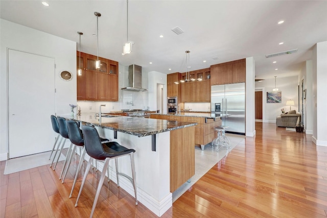 702 Crystal Mountain Dr, Austin, TX 78733 - kitchen with built in appliances, wall chimney range hood, light wood-style flooring, a peninsula, and a kitchen breakfast bar