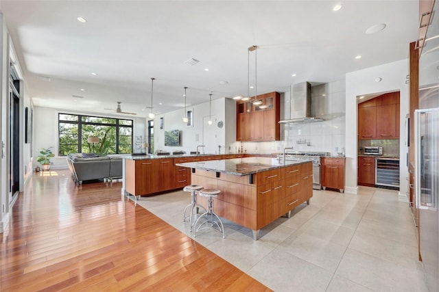 702 Crystal Mountain Dr, Austin, TX 78733 - kitchen with wall chimney exhaust hood, wine cooler, stainless steel range, open floor plan, and brown cabinetry
