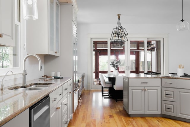 kitchen with sink, white cabinetry, dishwasher, hanging light fixtures, and light stone countertops