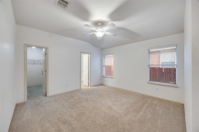 unfurnished bedroom featuring lofted ceiling, light colored carpet, a closet, ceiling fan, and a spacious closet