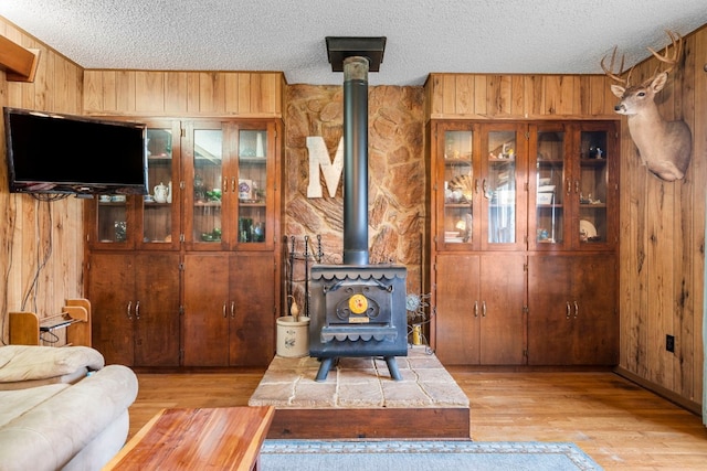 living room featuring light wood-type flooring, a wood stove, a textured ceiling, and wood walls