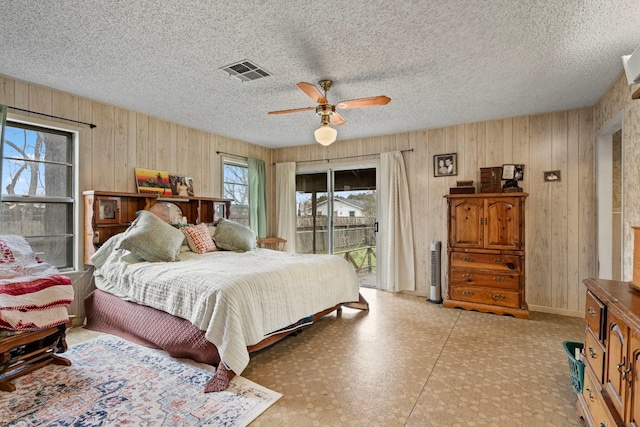 bedroom with ceiling fan, access to exterior, a textured ceiling, and wooden walls