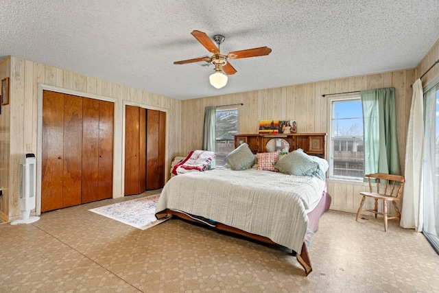 bedroom with wood walls, a textured ceiling, two closets, and ceiling fan