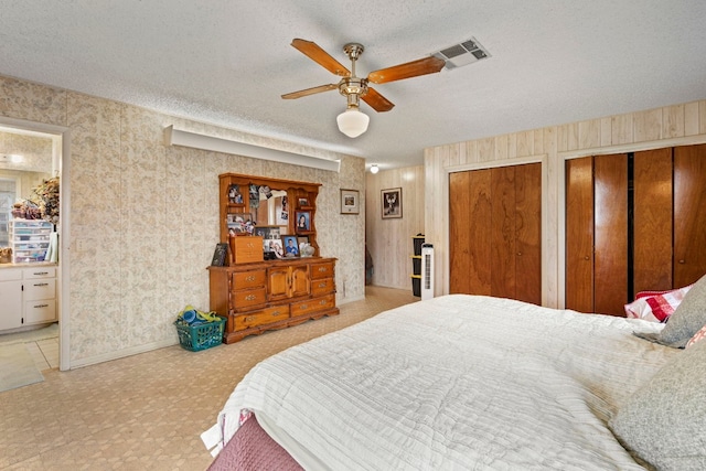 bedroom featuring ensuite bathroom, ceiling fan, multiple closets, and a textured ceiling