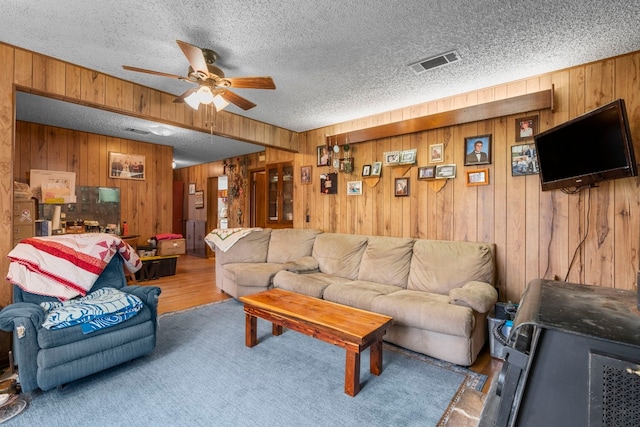 living room with hardwood / wood-style floors, ceiling fan, wood walls, and a textured ceiling