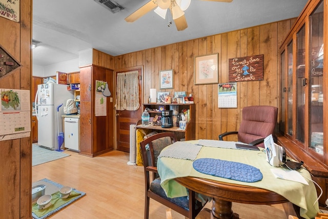 dining room with light hardwood / wood-style floors, ceiling fan, and wood walls