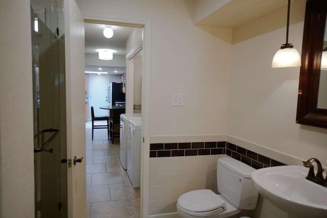 bathroom featuring sink, tile walls, washing machine and clothes dryer, toilet, and tile patterned floors