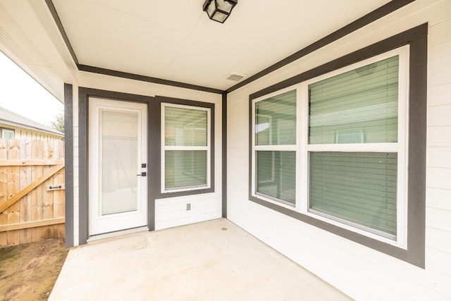 view of exterior entry with fence, visible vents, and a patio