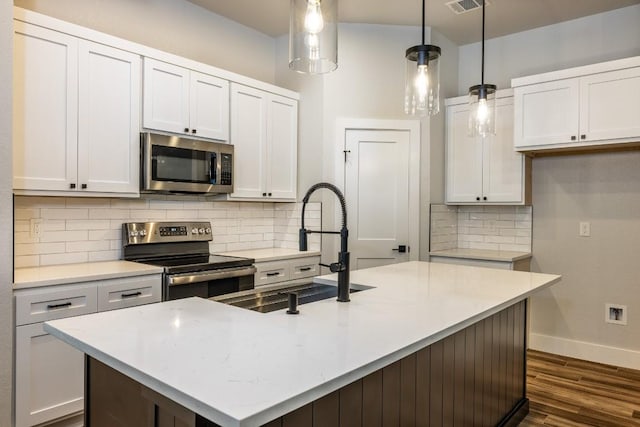 kitchen featuring hanging light fixtures, appliances with stainless steel finishes, light countertops, and an island with sink