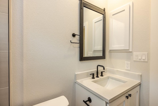 half bathroom with toilet, vanity, and a textured wall