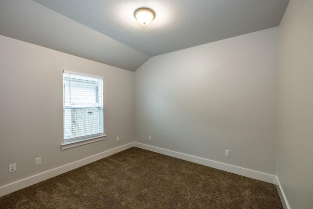 empty room featuring lofted ceiling, baseboards, dark carpet, and a textured ceiling