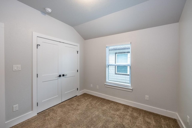 unfurnished bedroom with lofted ceiling, a closet, baseboards, and carpet flooring