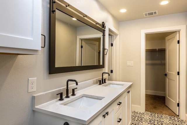 full bathroom featuring a walk in closet, visible vents, a sink, and double vanity