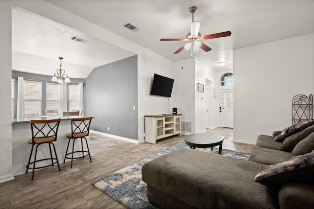 living room with ceiling fan with notable chandelier, vaulted ceiling, and wood-type flooring