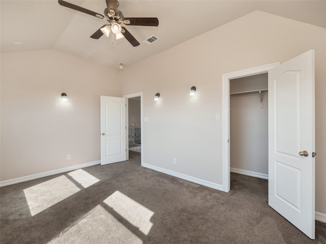 unfurnished bedroom with vaulted ceiling, a walk in closet, a closet, ceiling fan, and dark colored carpet