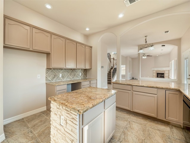 kitchen with ceiling fan, light stone countertops, a center island, and backsplash