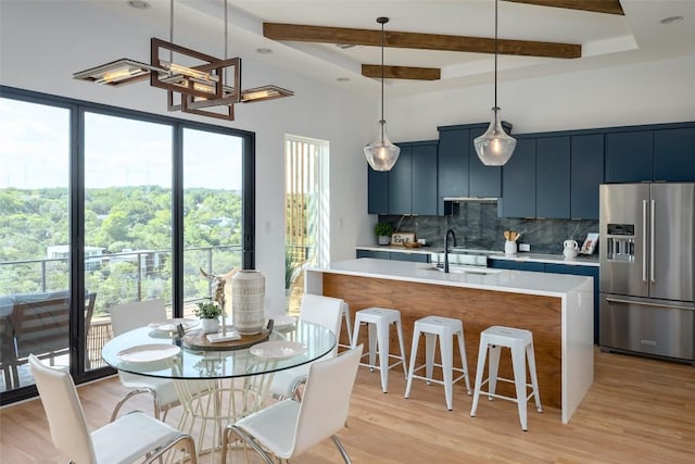 kitchen featuring a center island with sink, hanging light fixtures, blue cabinets, high quality fridge, and sink