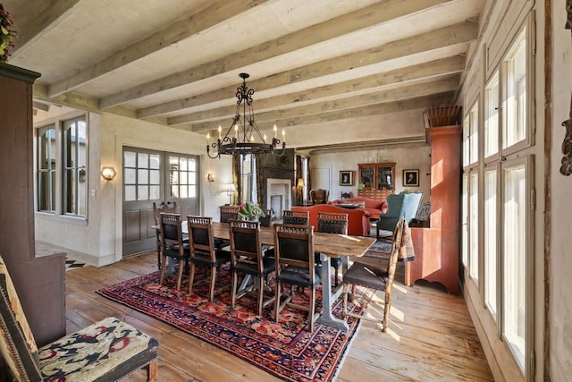 dining area with beam ceiling, light wood-style flooring, and an inviting chandelier