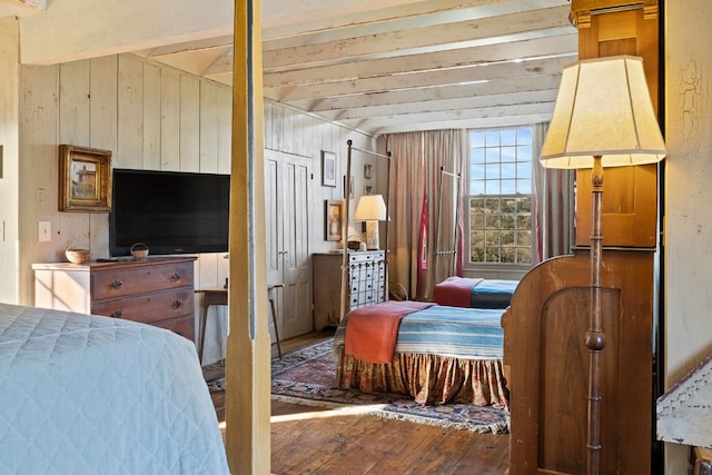 bedroom featuring wooden walls, wood finished floors, and beamed ceiling