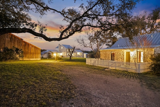 property exterior at dusk with metal roof, a lawn, and fence