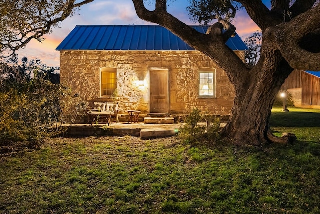 view of front of house with metal roof, a patio, stone siding, a yard, and a standing seam roof