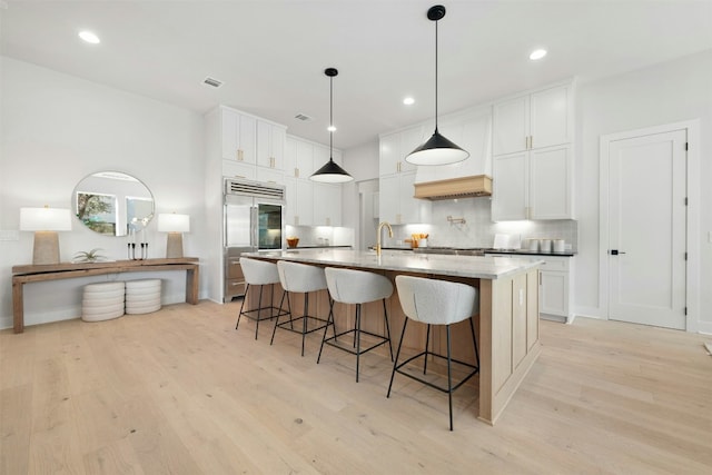 1339 Allen Rd, Austin, TX 78746 - kitchen featuring stainless steel built in refrigerator, light wood finished floors, a kitchen bar, a large island with sink, and white cabinets