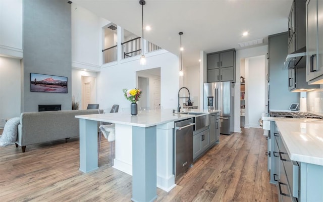 kitchen featuring appliances with stainless steel finishes, an island with sink, light stone counters, a large fireplace, and pendant lighting