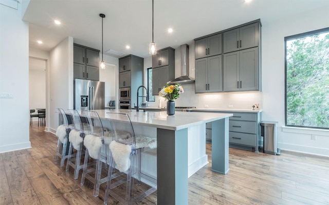 5408 Destination Way, Jonestown, TX 78645 - kitchen featuring wall chimney range hood, stainless steel appliances, gray cabinets, light wood finished floors, and healthy amount of natural light