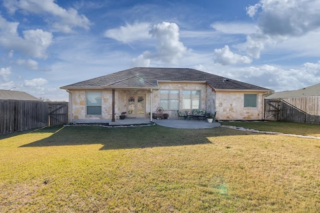 back of house featuring stone siding, a fenced backyard, a gate, a yard, and a patio area