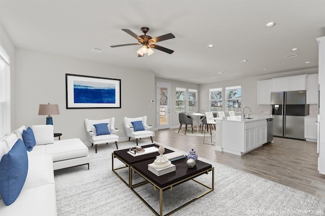 living room with ceiling fan, sink, and light wood-type flooring