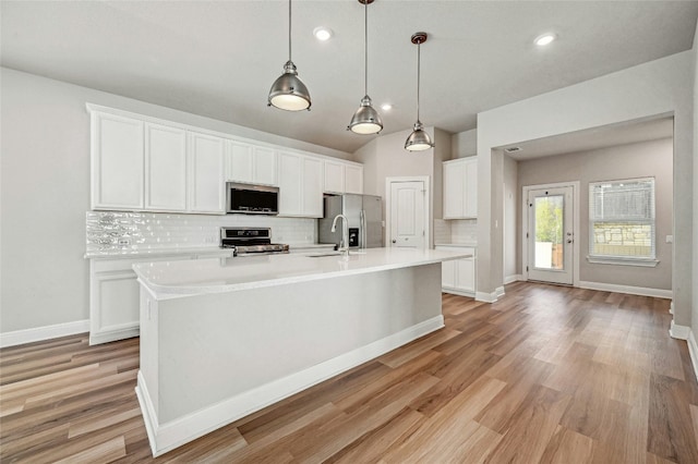 kitchen featuring white cabinets, hanging light fixtures, stainless steel appliances, and a kitchen island with sink