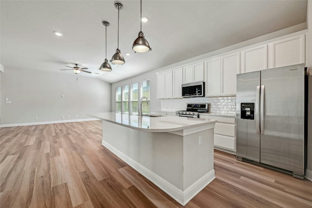 kitchen with a center island with sink, sink, decorative light fixtures, stainless steel appliances, and white cabinets