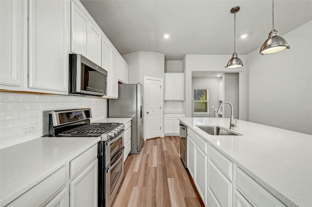 kitchen featuring sink, light wood-type flooring, white cabinetry, stainless steel appliances, and hanging light fixtures