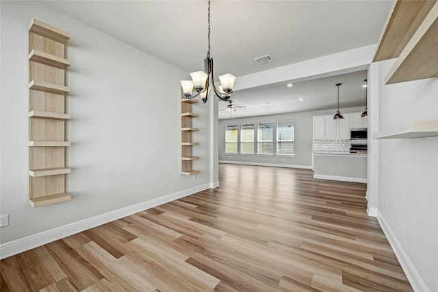 unfurnished dining area with ceiling fan with notable chandelier and light wood-type flooring