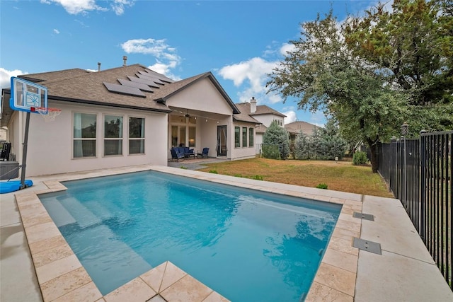 rear view of property featuring a fenced in pool, a lawn, solar panels, a patio area, and ceiling fan