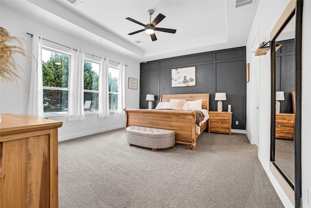 carpeted bedroom featuring a tray ceiling and ceiling fan