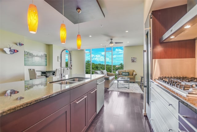 kitchen with hanging light fixtures, light stone countertops, sink, appliances with stainless steel finishes, and wall chimney range hood