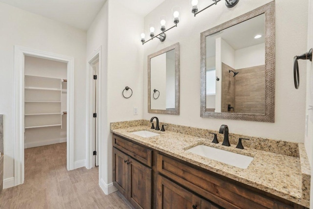 full bathroom featuring wood finished floors, a sink, a walk in closet, and a tile shower