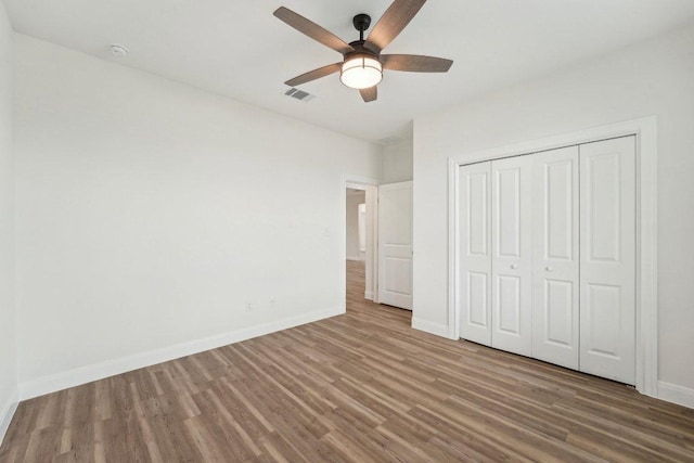 unfurnished bedroom with baseboards, wood finished floors, visible vents, and a closet