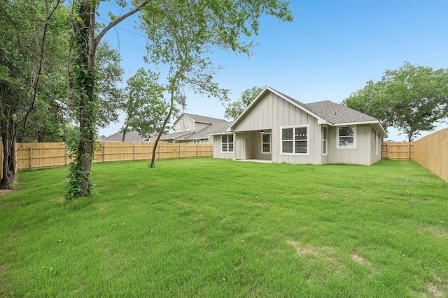 back of house with board and batten siding, a yard, a shingled roof, and a fenced backyard