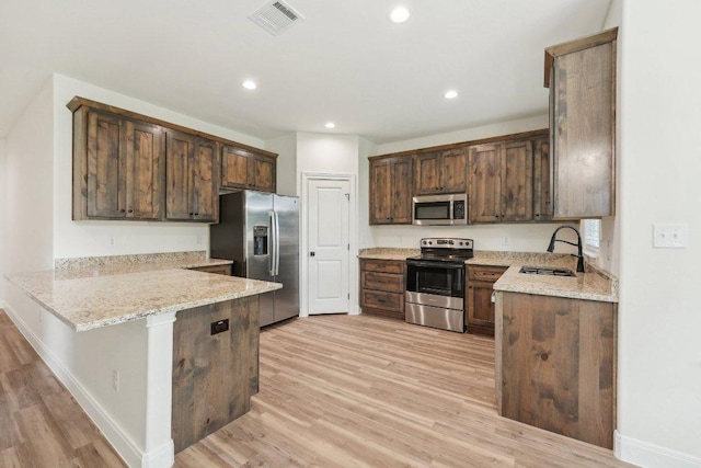 kitchen featuring a sink, stainless steel appliances, light wood-style flooring, a peninsula, and light stone countertops